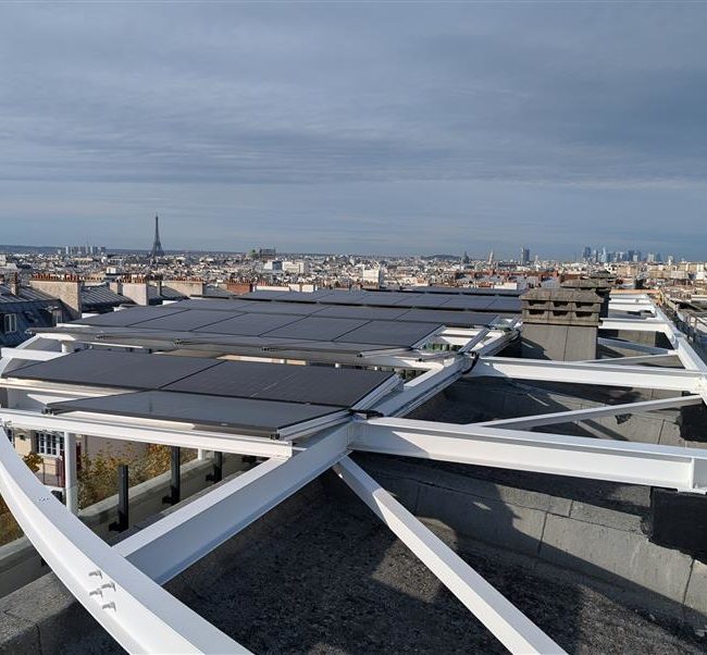 Vue d’une toiture ombrière équipée de panneaux photovoltaïques au sein d’une école primaire située dans le 10ᵉ arrondissement de Paris, avec une vue sur tout Paris.